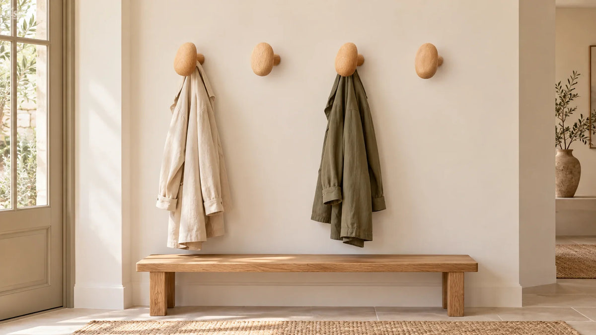 Quatre patères en bois espacées sur un mur d’entrée