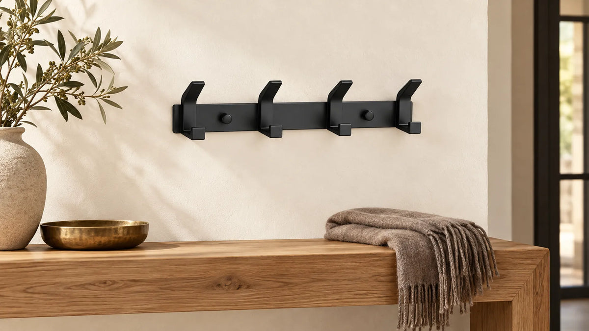 Barre noire à quatre doubles crochets sur un mur clair, au-dessus d’une console