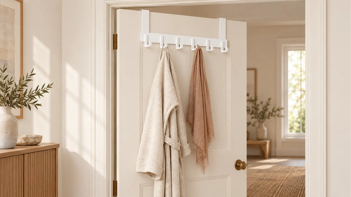 Porte-manteau blanc à six crochets suspendu sur une porte entrouverte dans une entrée beige