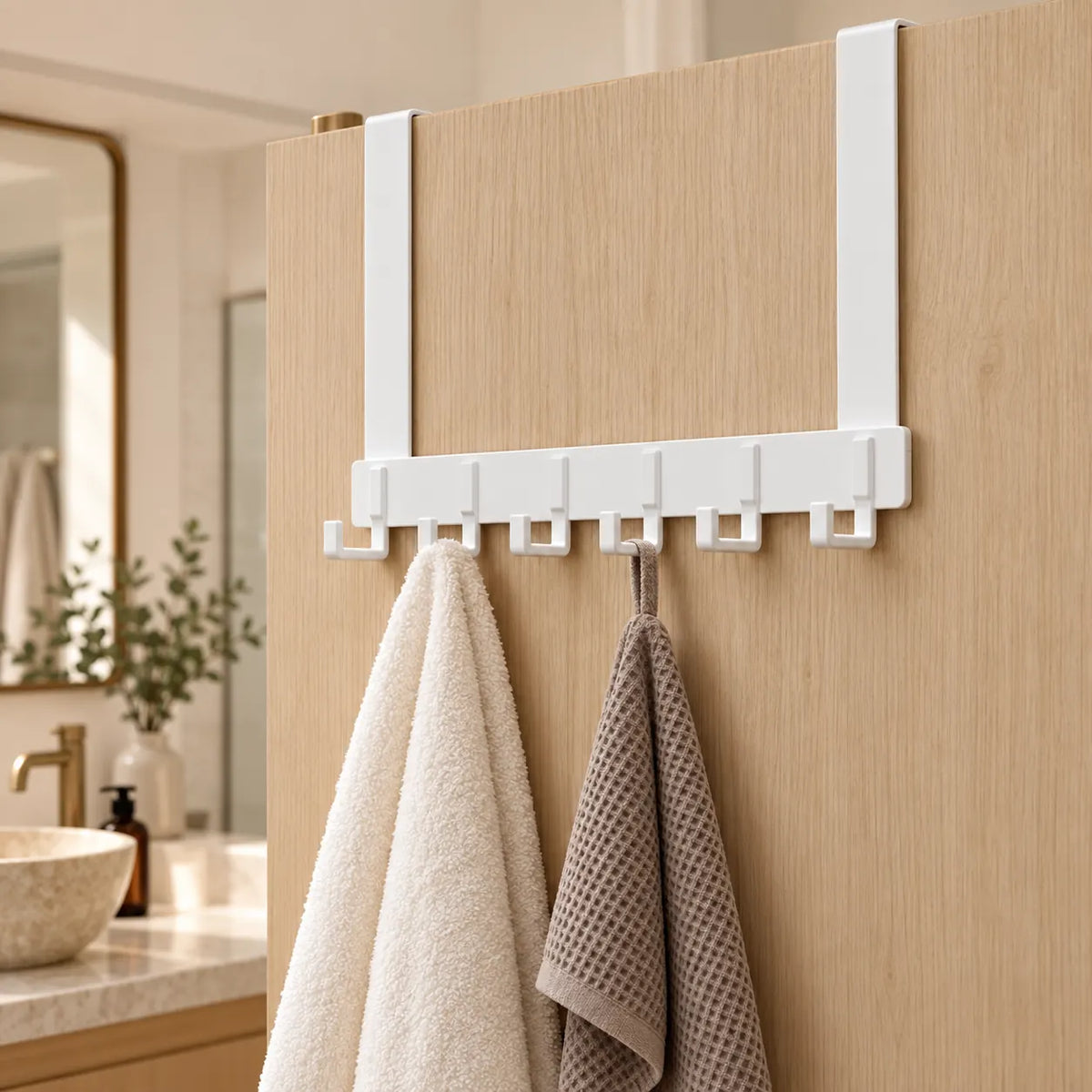 Porte-serviettes blanc à six crochets sur une porte dans une salle de bain beige et bois.