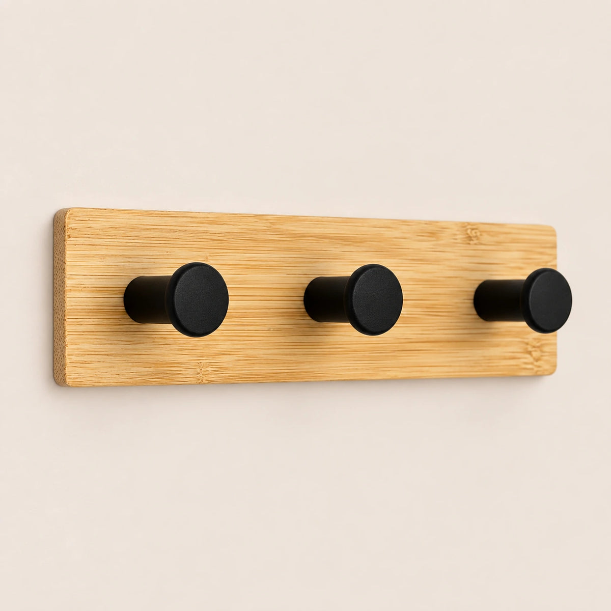 Patère murale en bambou naturel avec trois crochets noirs, présentée sur fond beige.