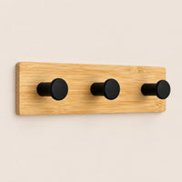 Patère murale en bambou naturel avec trois crochets noirs, présentée sur fond beige.