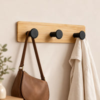 Patère murale bambou avec sac et vêtement léger suspendus dans une entrée beige.