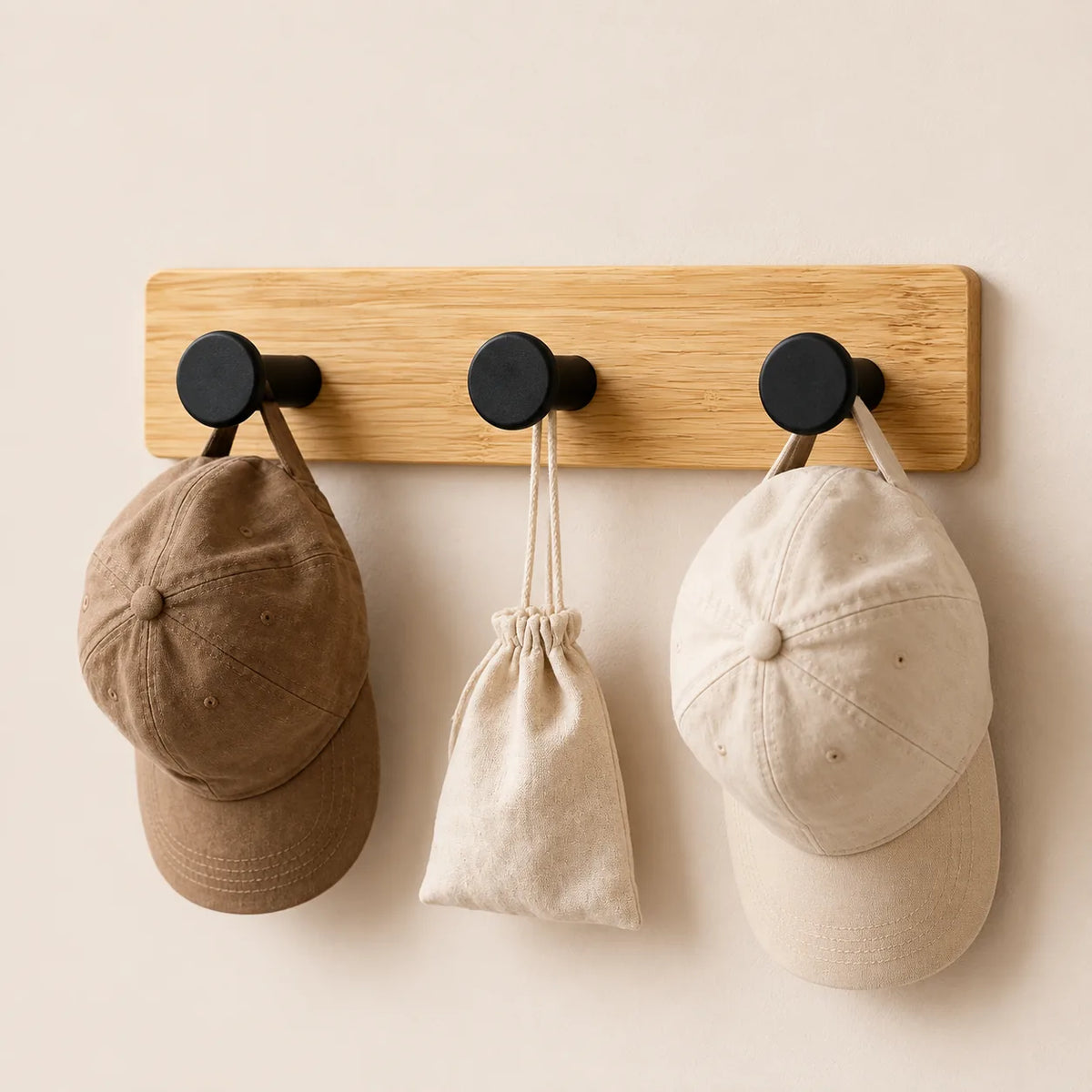Patère bambou à trois crochets noirs avec deux casquettes et une pochette en tissu.