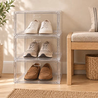 Trois boîtes à chaussures transparentes empilées dans une entrée beige.
